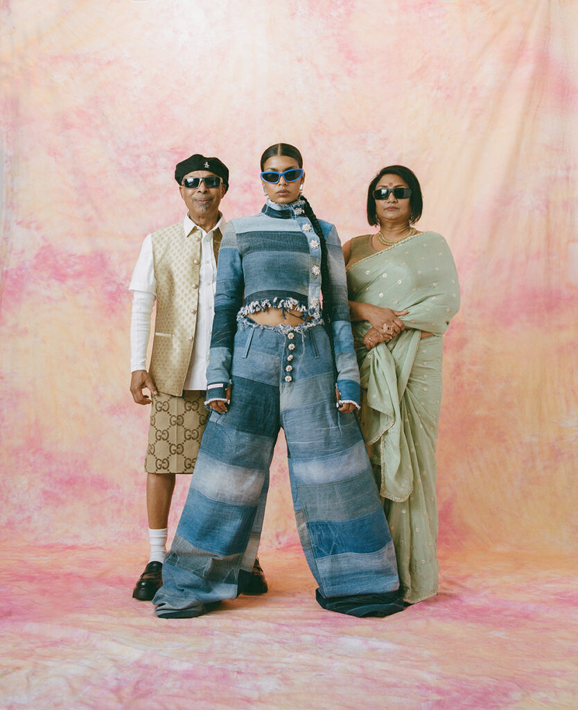 Pia Ahmed in einem Jeans-Zweiteiler, hinter ihr stehen ihre Eltern aus Bangladesch.